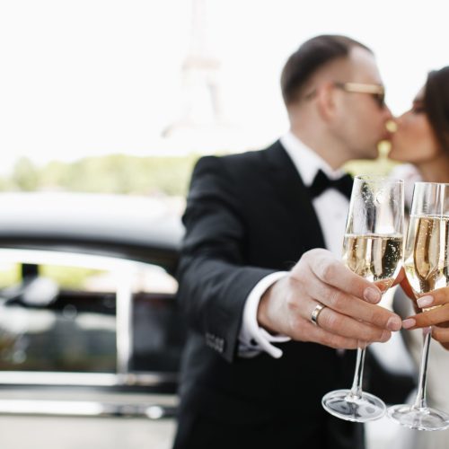 Newlyweds drink champagne standing before a retro car